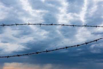 fence of barbed wire against the background of a beautiful blue sky.rusty fence of barbed wire fence at jail or border.