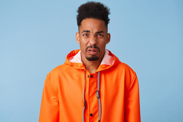 Close up of dissatisfied young african american dark skinned male wears in orange rain coat, frowns...