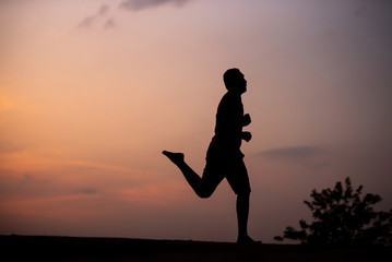 Man running alone at beautiful sunset in the road at park . Summer sport and freedom concept. Athlete training on dusk. - Image