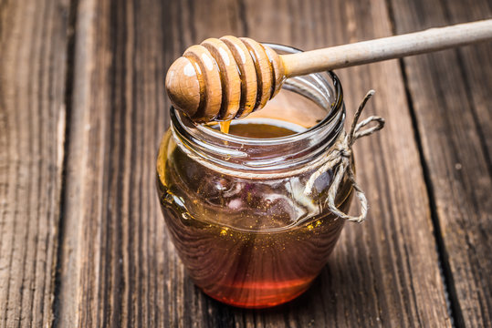 Glass jar of honey and dipper on wooden background