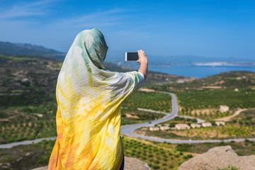 Muslim woman  traveler in a colorful scarf  take self portrait on the smartphone on top of a mountain.