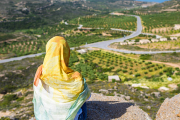 A lonely Muslim woman  traveler in a colorful scarf sits on top of a mountain.
