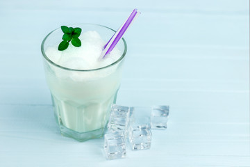 glass of milkshake with ice cubes and mint  on blue wood background