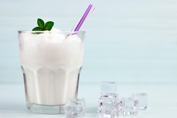 glass of milkshake with ice and mint on light wood background
