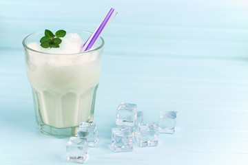 glass of milkshake with ice cubes and mint  on blue wood background