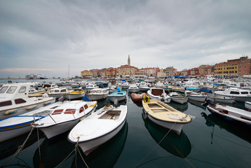 Fototapeta na wymiar Rovinj, Croatia. Motorboats and boats on water in port of Rovinj. Medieval vintage houses of old town. Yachts landing, tower with clock on the background.