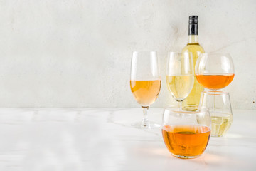 Trendy orange wine, with white wine in different glasses, white concrete background copy space