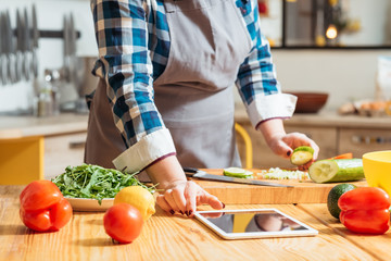 Healthy diet. Woman watching online culinary class on her tablet, making salad with fresh vegetables. Vegetarian food.