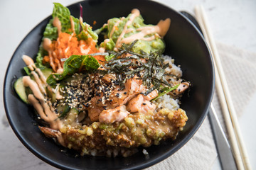 Poke Bowl mit flambierten Lachs, Tempura Shrimp, Guacamole, Masago Kaviar, Salat, Nori Algen und Sesam auf Reis in schwarz Porzellan Schale