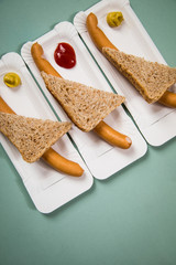Drei Wiener Würstchen mit Vollkorn Brot Scheibe auf Einweg Pappteller mit Senf und Ketchup auf Hintergrund Grün