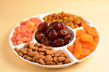 Mix of dried fruits and nuts on a white plate. Apricot, almond, raisin, dates fruit. On a beige background. Space for text or design.