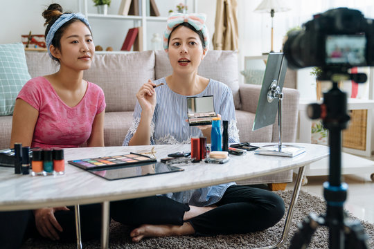 Beautiful asian woman blogger showing how to make up and use cosmetics. young girl vlogger friend together recording makeup tutorial video by professional camera in living room at home sit on carpet - Powered by Adobe