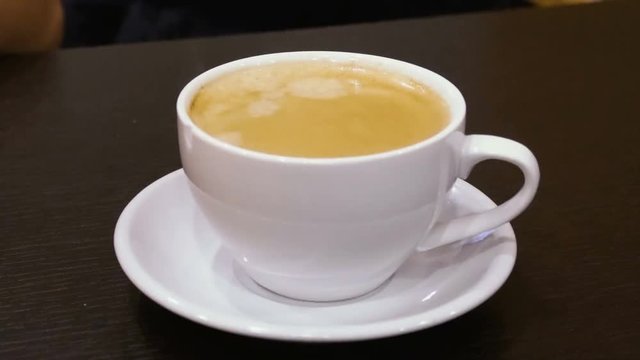 White mug with hot cappuccino coffee on the table. Steam rises up. Mug close up.