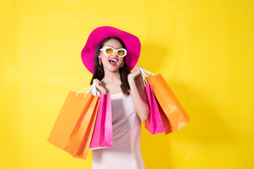 Portrait of a happy Asian pretty girl holding shopping orange bags away isolated over yellow background,colorful shopping concept. -