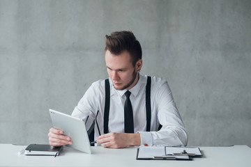 Corporate lifestyle. Portrait of young office manager sitting at desk, using tablet. Serious facial expression. Copy space.