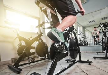 Wide angle view of man in sports sneakers and shorts does exercises on cardio bike at spinning class. Healthy lifestyle concept