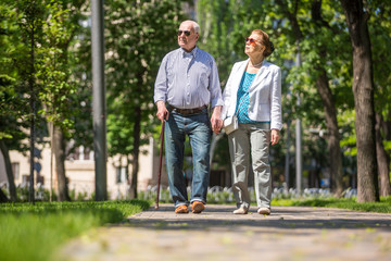Obraz premium Cheerful senior couple having good time in city park, walking, laughing and enjoying sunny day. Old people wearing color clothes ans sunglasses