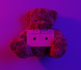 Music lover concept Teddy bear hold audio cassette in red blue neon light. Top view. Retro style 80s. Minimalism