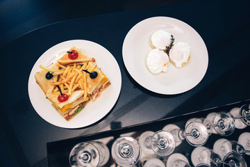 sandwich with french fries. poached eggs. male breakfast. white plate on black table