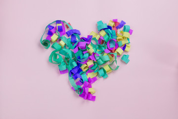 Bright multi-colored heart from paper confetti on a pink background
