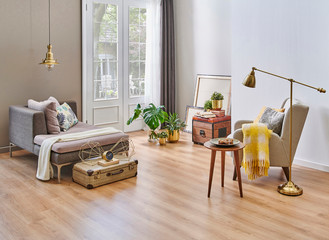 Modern living room grey sofa and armchair with yellow blanket, carpet detail on the parquet, gold vase of flower and lamp.