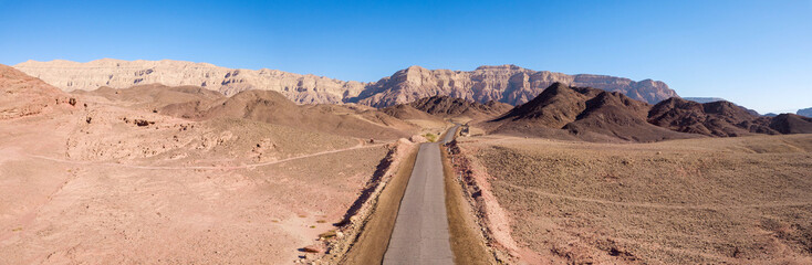 Long stretch of an old Desert road with mountains and blue sky in the background, Aerial image.