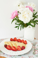 Obraz na płótnie Canvas pancakes with strawberries and coffee on the table near a vase with peonies on a white background