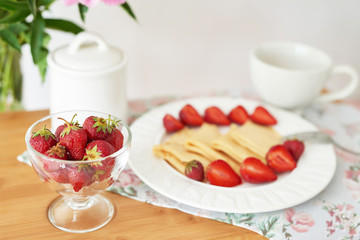 Fototapeta na wymiar pancakes with strawberries and coffee on the table near a vase with peonies on a white background