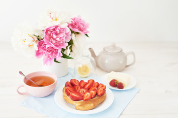 strawberry with croissant and tea on the table near a vase with peonies on a white background