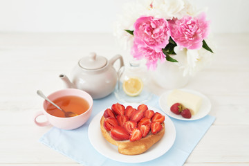 strawberry with croissant and tea on the table near a vase with peonies on a white background