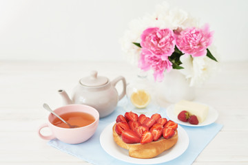 strawberry with croissant and tea on the table near a vase with peonies on a white background