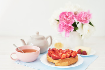 strawberry with croissant and tea on the table near a vase with peonies on a white background