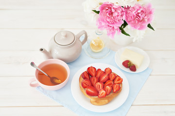strawberry with croissant and tea on the table near a vase with peonies on a white background