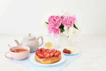 Fototapeta na wymiar strawberry with croissant and tea on the table near a vase with peonies on a white background