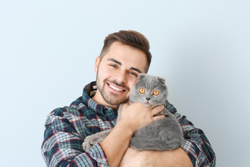 Young man with cute funny cat on light background