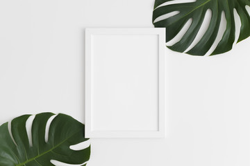 Top view of a white frame mockup with monstera leaf decoration. Portrait orientation.