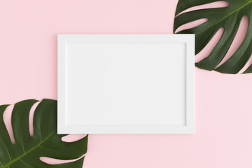 Top view of a white frame mockup with monstera leaf decoration on a pink background. Landscape...