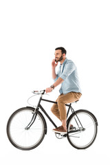 Fototapeta na wymiar smiling bearded man riding bicycle and talking on smartphone isolated on white
