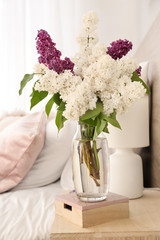 Vase with beautiful lilac flowers on table in bedroom