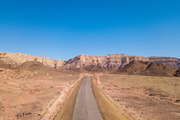 Long stretch of an old Desert road with mountains and blue sky in the background, Aerial image.