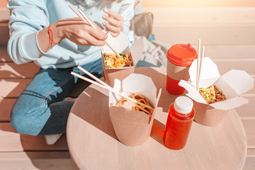 Fashionable asian teen hipster girl eats Oriental wok noodles with chopsticks. Concept of lunch and natural takeaway containers made of paper