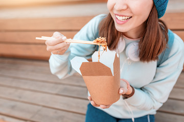 Fashionable asian teen hipster girl eats Oriental wok noodles with chopsticks. Concept of lunch and...