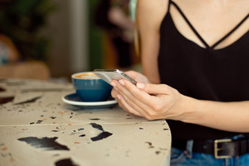 Fototapeta na wymiar Close-up of female hands holding a cell phone, girl sits in a cozy cafe drinking coffee watching videos on a mobile phone during a break