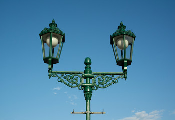 Fototapeta na wymiar Retro vintage lamp and lantern is made of cast iron. Historical illumination on the street during sunny daylight, clear blue sky in the background.