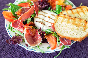 Tasty mixed salad dish with grilled camembert cheese, prosciutto ham, organic tomato and fresh green leaves. Healthy dilicious meal. Isolated on black