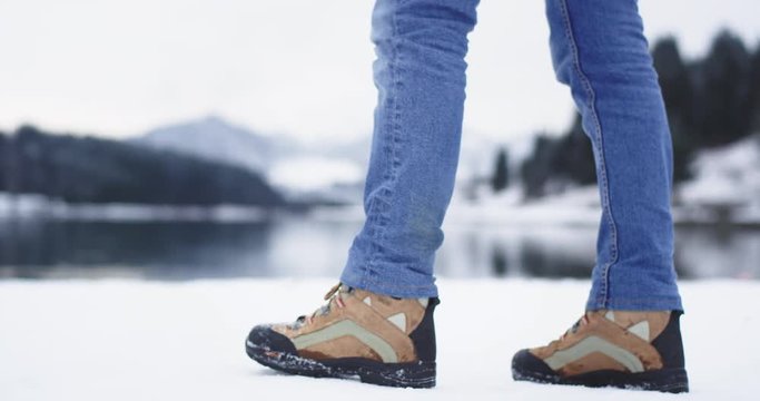 Tourist details of legs walking around the shore lake , tourist wearing jeans and mountain boots