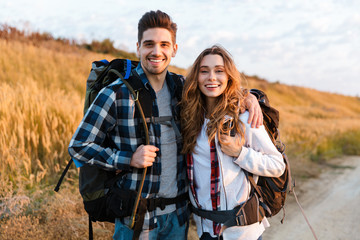 Cheerful young couple carrying backpacks hiking together