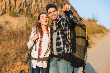 Cheerful young couple carrying backpacks hiking together