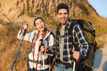 Cheerful young couple carrying backpacks hiking together