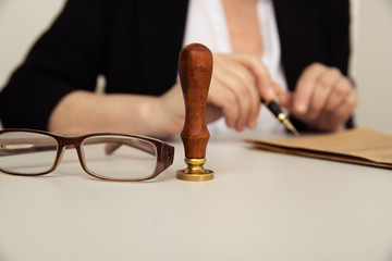 Female hand with pen and notary paper. Glasses and stamp on the desk